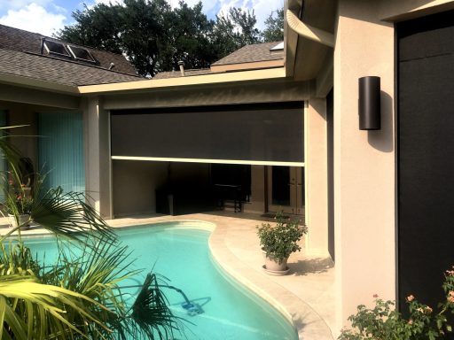 A poolside view featuring dark retractable screens and surrounding greenery.